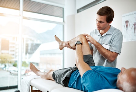 Arbeiten im Gesundheitswesen: Ein Physiotherapeut behandelt einen älteren Mann am Knie