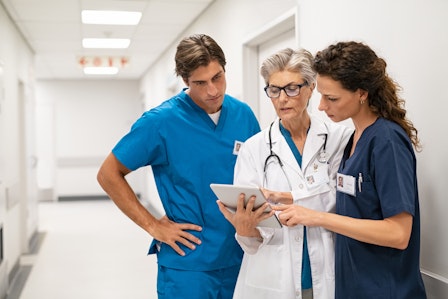 Eine Ärztin betrachtet mit zwei Medizinern medizinische Daten auf dem Tablet