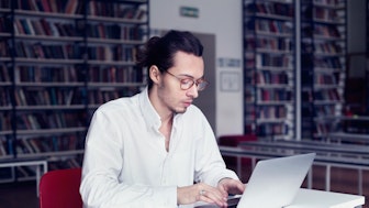 Ein Doktorand am Laptop in einer Bibliothek
