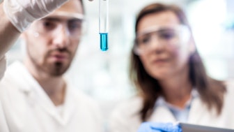 Ein Chemiker und eine Chemikerin im Labor mit einem Reagenzglas mit leuchtend blauer Flüssigkeit