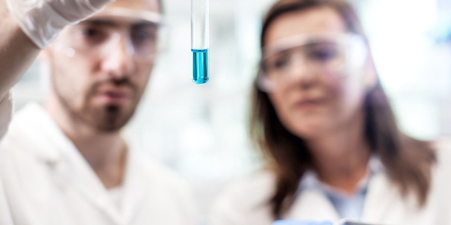 Ein Chemiker und eine Chemikerin im Labor mit einem Reagenzglas mit leuchtend blauer Flüssigkeit