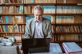 Digital Humanities: Ein Mann in einer Bibliothek mit alten Büchern am Laptop