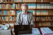 Digital Humanities: Ein Mann in einer Bibliothek mit alten Büchern am Laptop