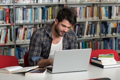 Ein junger Mann schreibt in der Bibliothek an seiner Doktorarbeit