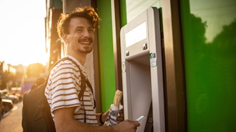 Ein junger Mann am Geldautomat freut sich über sein Gehalt im öffentlichen Dienst