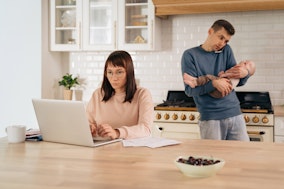 Job und Familie: Eine Frau am Laptop und ein Mann mit Handy am Ohr und Kind auf dem Arm in der Küche
