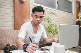 Ein junger Mann macht konzentriert Notizen für sein Forschungsexposé
