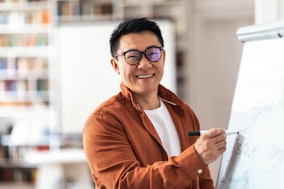Ein asiatischer, lächelnder Dozent an einem Whiteboard