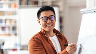 Ein asiatischer, lächelnder Dozent an einem Whiteboard