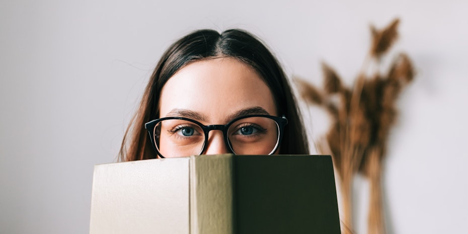 Germanistik: Eine Frau mit Brille schaut hinter einem Buch hervor