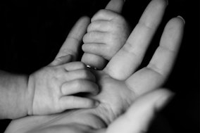 Hand eines Neugeborenen und eines Erwachsenen als Symbolbild für den Verdienst von Hebammen