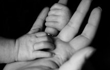 Hand eines Neugeborenen und eines Erwachsenen als Symbolbild für den Verdienst von Hebammen