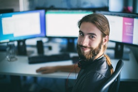 Ein lächelnder Informatiker vor seinen Bildschirmen beim Programmieren