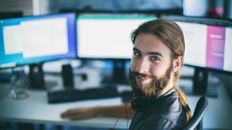 Ein lächelnder Informatiker vor seinen Bildschirmen beim Programmieren