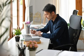 Ein asiatisch aussehender Mann macht sich Notizen für seine Bewerbung als Postdoc