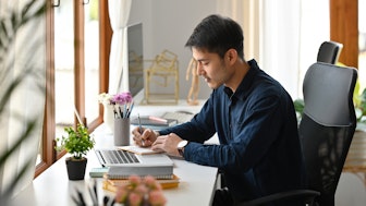 Ein asiatisch aussehender Mann macht sich Notizen für seine Bewerbung als Postdoc