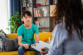 Eine Psychologin in Gespräch mit einem Teenager, der auf einem gelben Sofa sitzt
