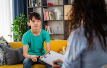 Eine Psychologin in Gespräch mit einem Teenager, der auf einem gelben Sofa sitzt