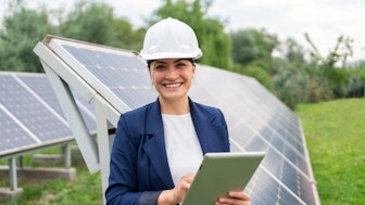 Eine Umweltingenieurin mit Schutzhelm und Tablet vor einer Solaranlage