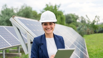 Eine Umweltingenieurin mit Schutzhelm und Tablet vor einer Solaranlage