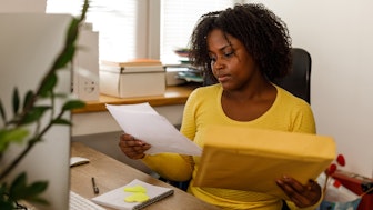 Unterlagen nachreichen: Geschäftsfrau entnimmt Papiere aus einem Umschlag